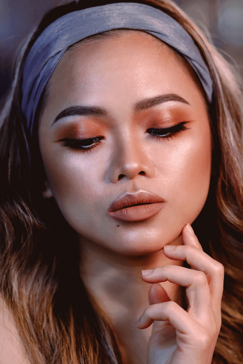 Young woman with elegant makeup, wearing a headband, thoughtful expression, hand on chin.