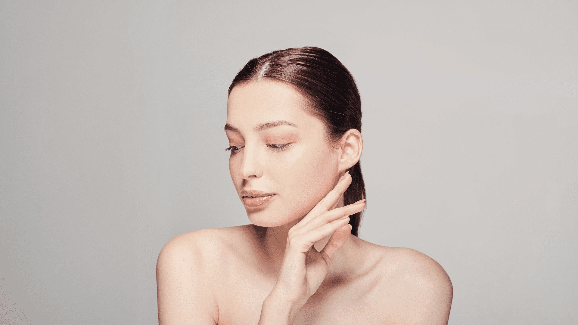 Woman with smooth skin posing with hand near face against a neutral background.