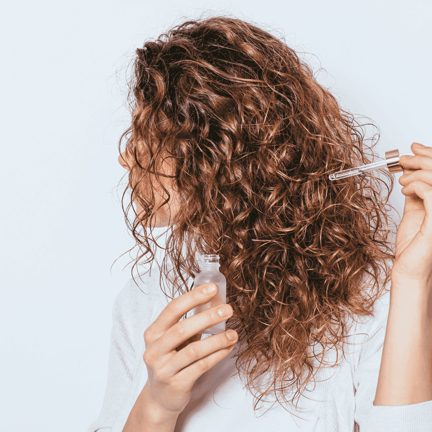 Curly-haired person applying serum with a dropper.
